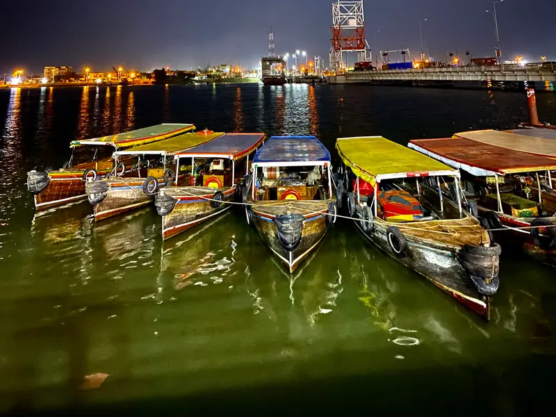 Traditional passenger boats moored on the Shatt al-Arab at night, the Basra skyline behind